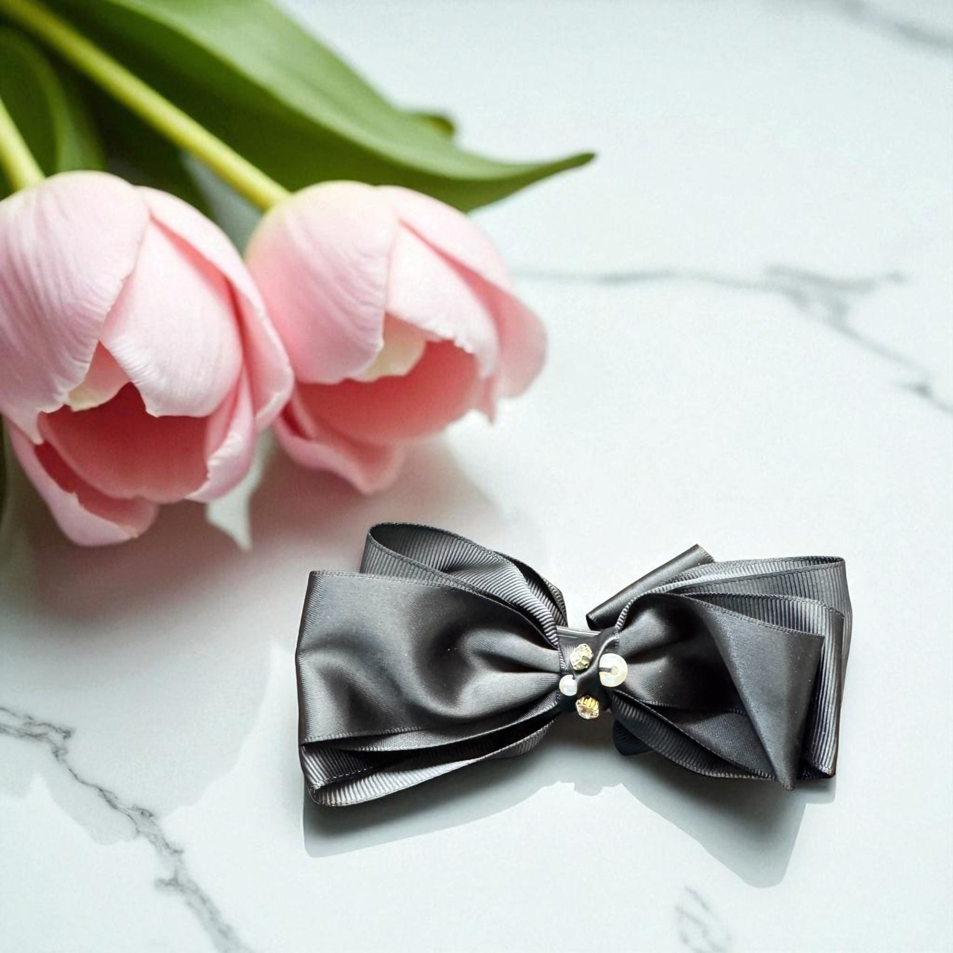Black bow with gold accents on a marble surface with pink tulips