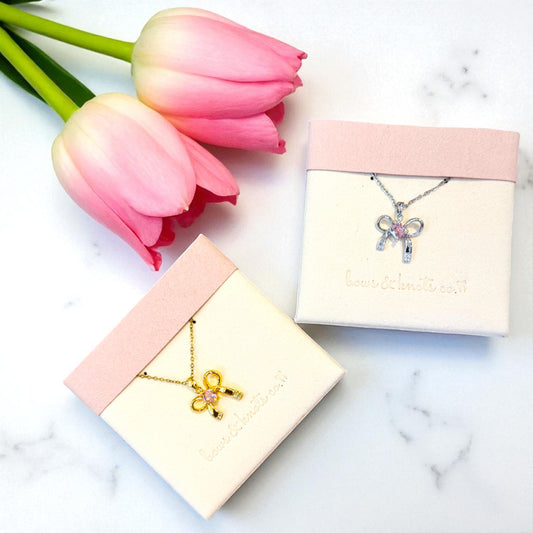 Two bowknot necklaces in display boxes with pink tulips on a marble surface