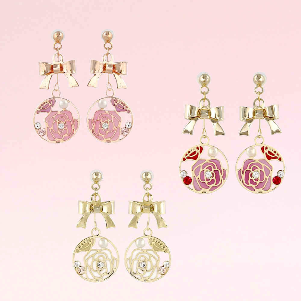 Pair of decorative earrings with floral and bow designs on a pink background