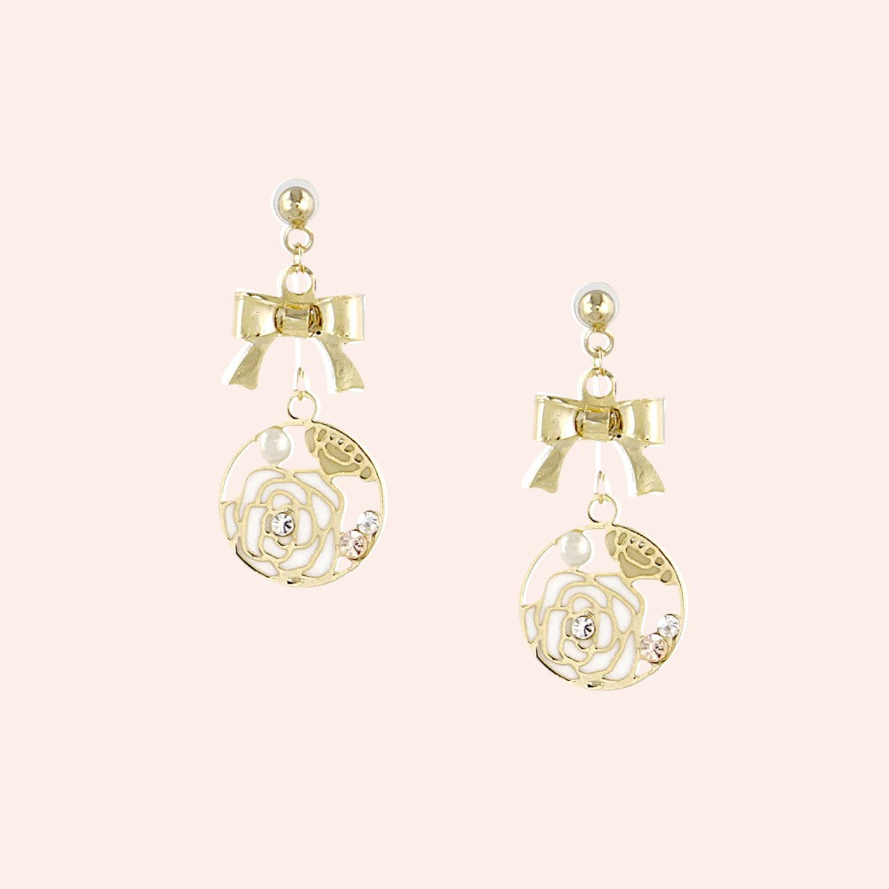 Gold earrings with bow and rose design on a light pink background