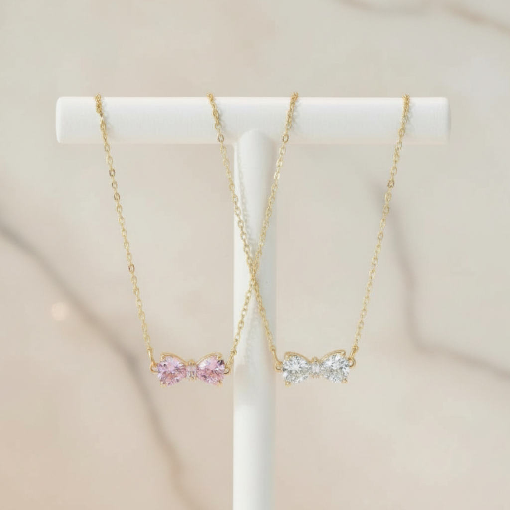 Two gold necklaces with pink and clear gemstones on a white stand against a beige background.