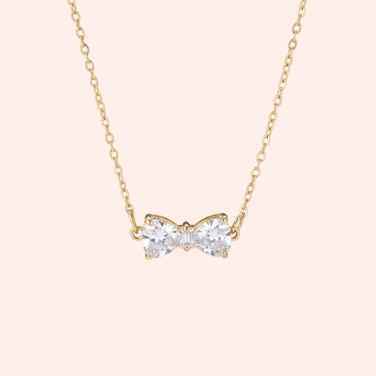 Gold necklace with a bow-shaped pendant on a light pink background
