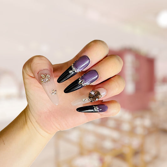 Hand with black and purple nail art featuring decorative elements on a blurred background
