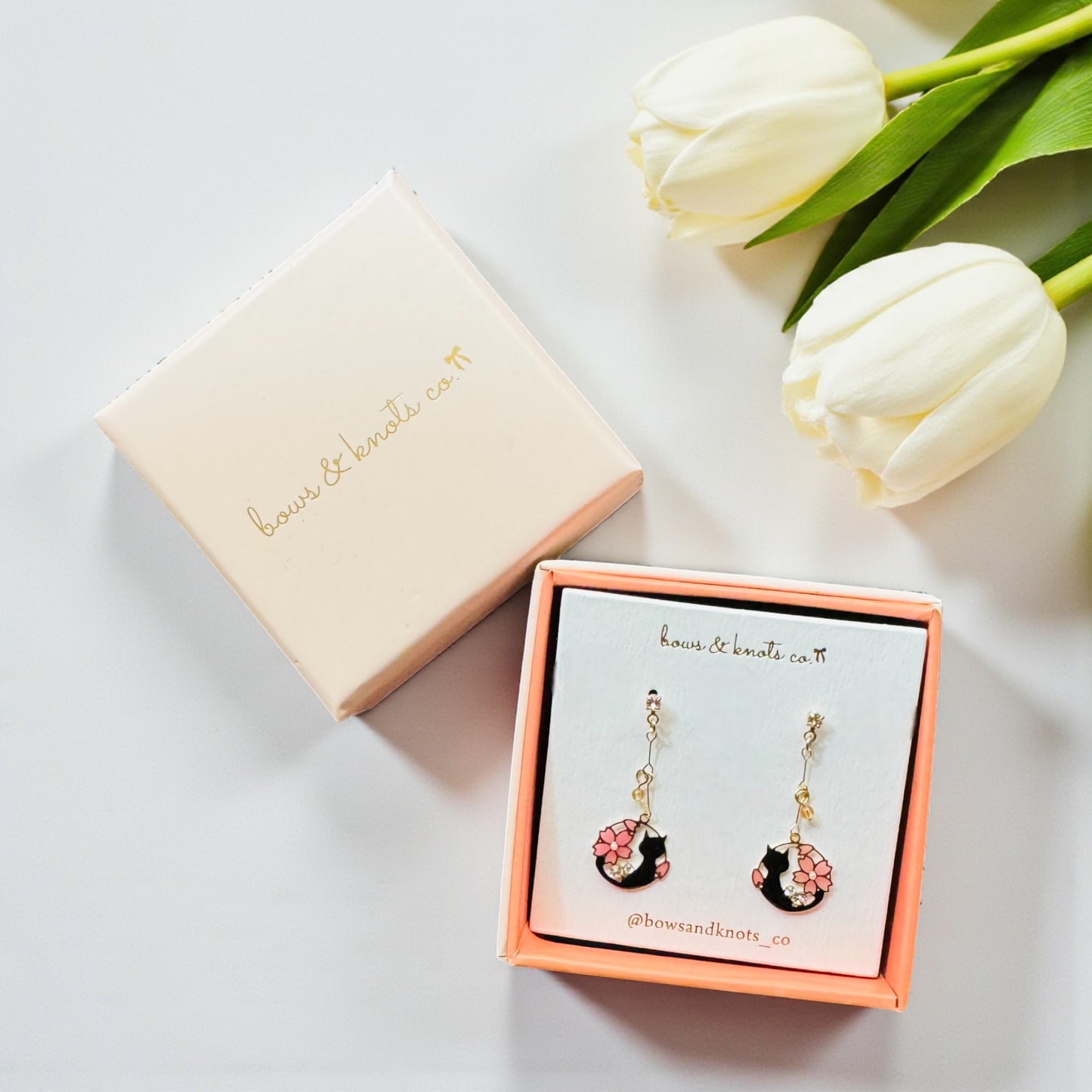 Pair of earrings in a box with white tulips on a light background