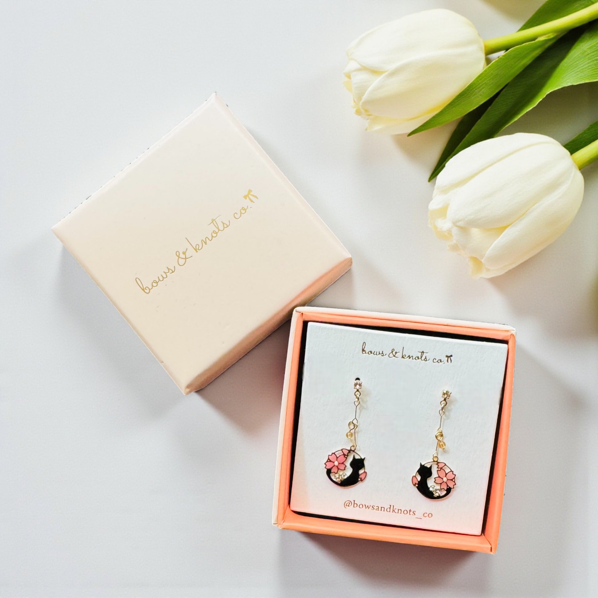 Pair of earrings in a box with white tulips on a light background