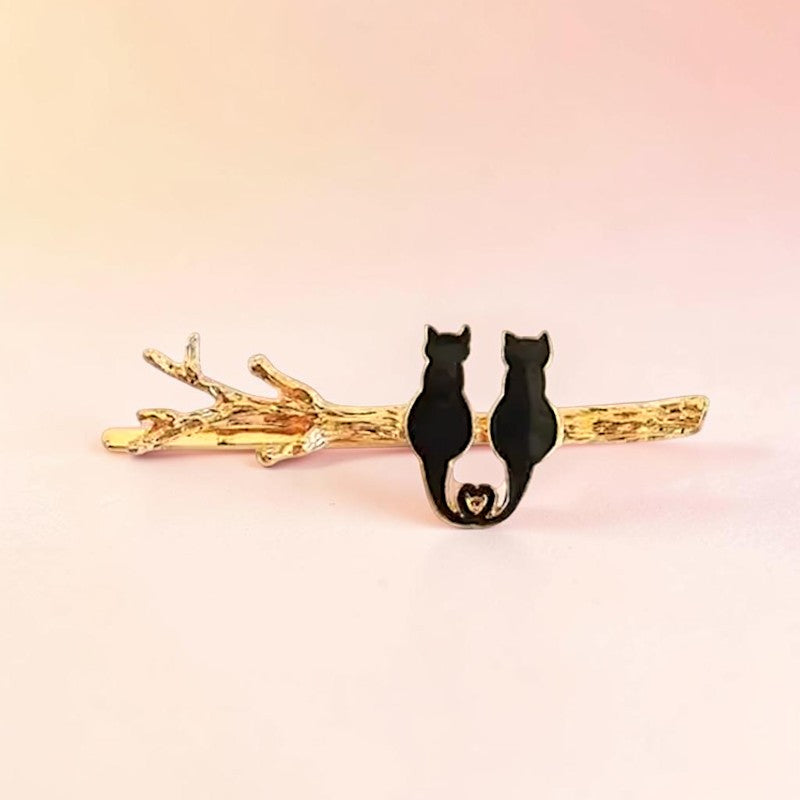 Black cat-shaped hair clip on a gold branch against a pink background