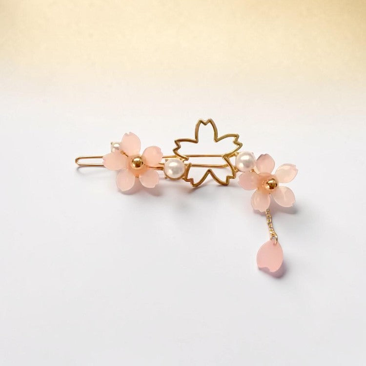 Decorative hair clip with pink flowers and a gold leaf on a light background