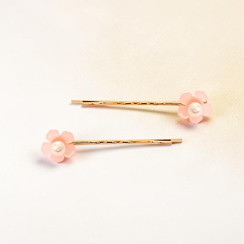 Two gold hair pins with pink flower designs on a light beige background