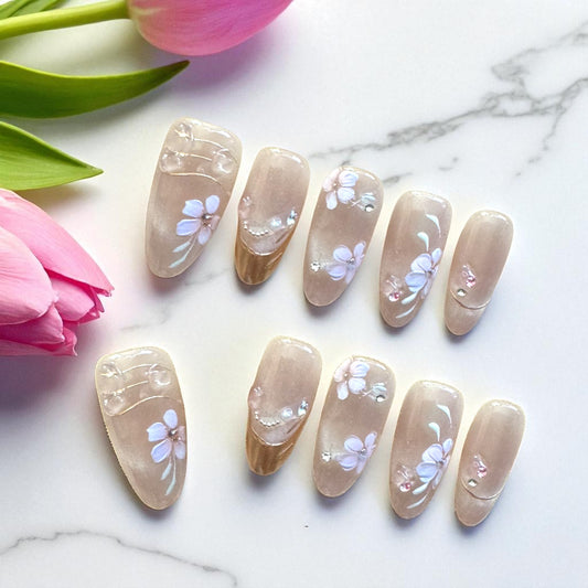 Nail art with floral designs on beige nails, placed on a marble surface with pink tulips.
