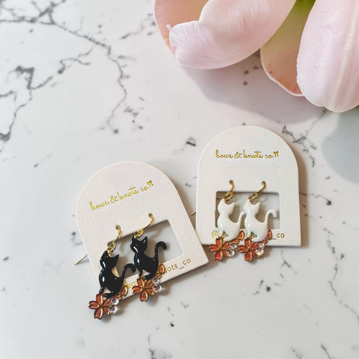 Pair of cat-themed earrings on a marble surface with a hand holding them.