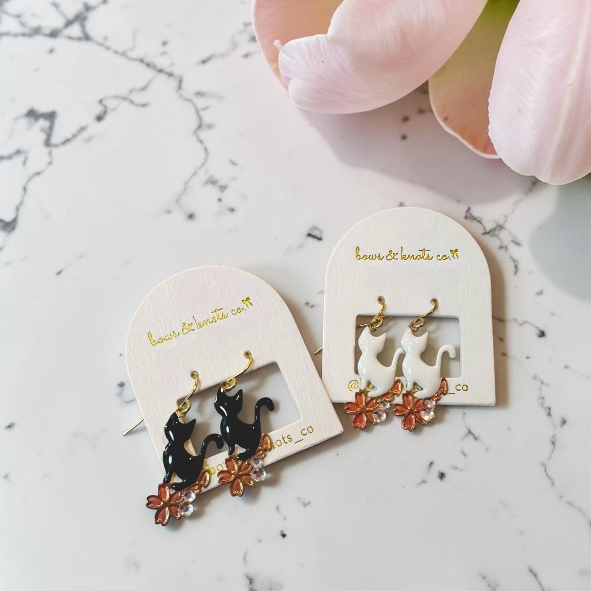 Pair of cat-themed earrings on a marble surface with a hand holding them.