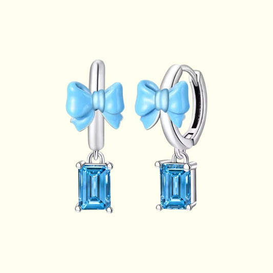 Pair of earrings with blue bow and gemstone design on a white background