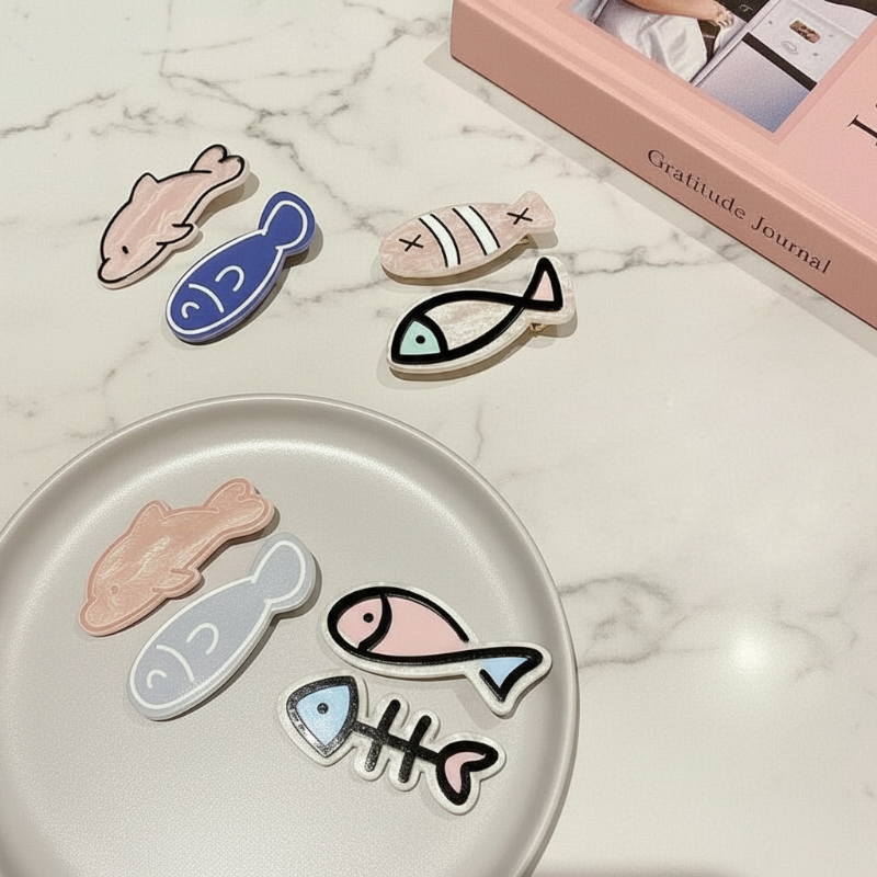 Set of fish-shaped hair clips on a marble surface with a gratitude journal in the background.