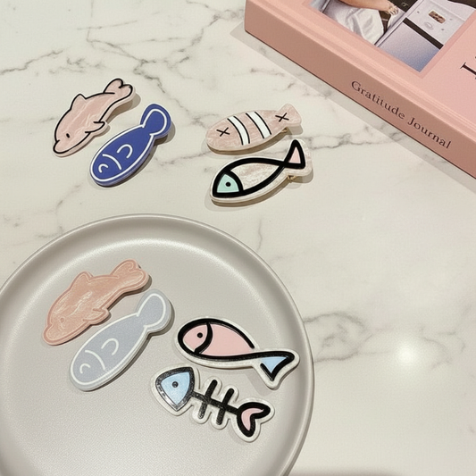 Set of fish-shaped hair clips on a marble surface with a gratitude journal in the background.