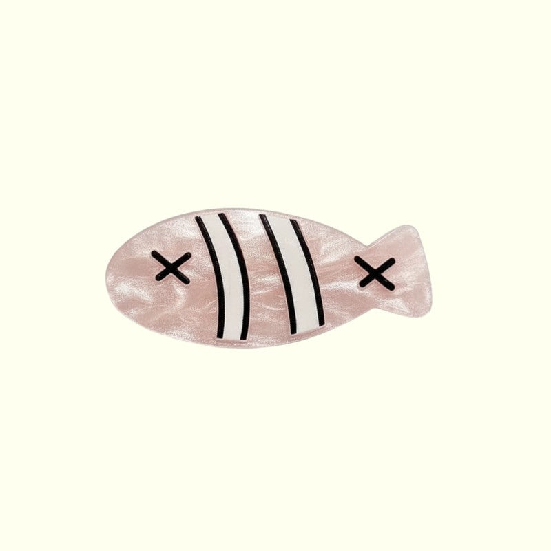 Pink fish-shaped hair clip with black stripes and crosses on a white background