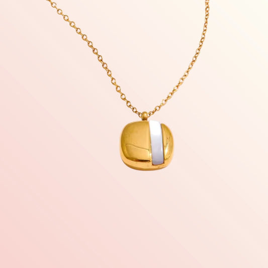 Gold necklace with a square pendant on a light pink background
