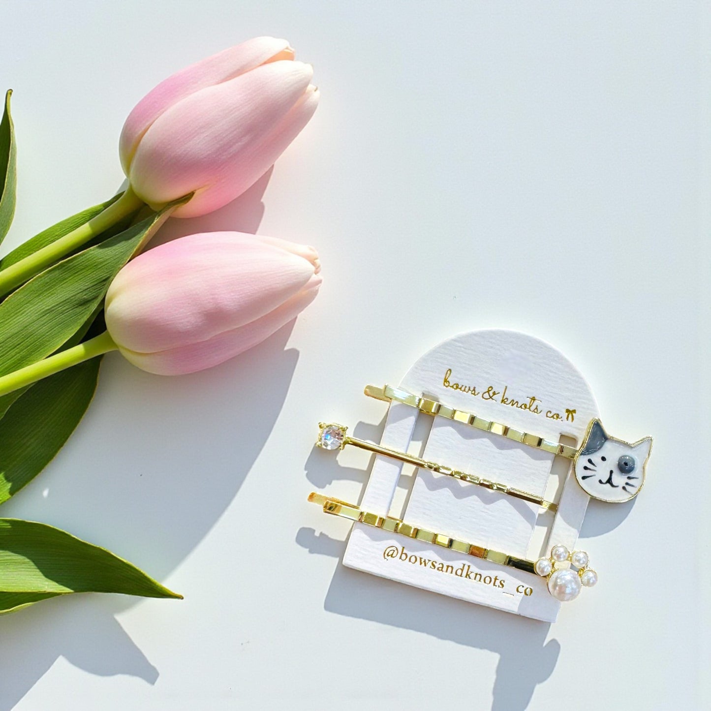 Gold hair accessories on a white stand with pink tulips on a light blue background