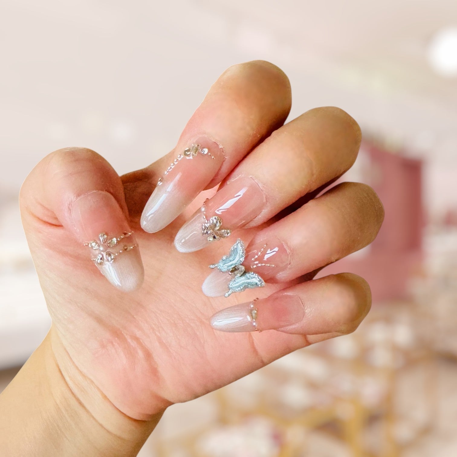 Hand with decorative nails featuring butterflies and rhinestones against a blurred background