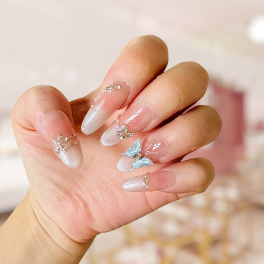 Hand with decorative nails featuring butterflies and rhinestones against a blurred background