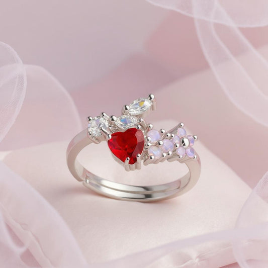 Silver ring with a red heart-shaped gemstone on a soft pink background