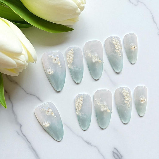 Set of light blue nail art designs with gold accents on a marble surface with white tulips.