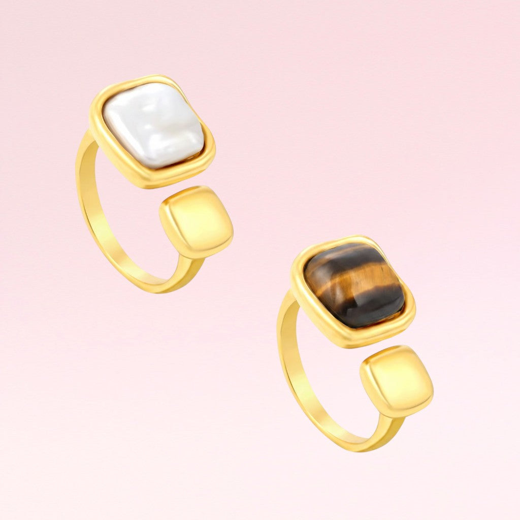 Two gold rings with gemstones on a pink background