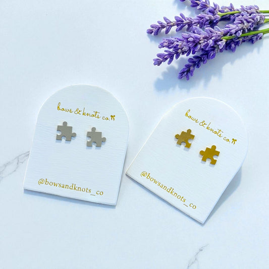 Silver puzzle piece earrings on branded card with lavender flowers on light blue background