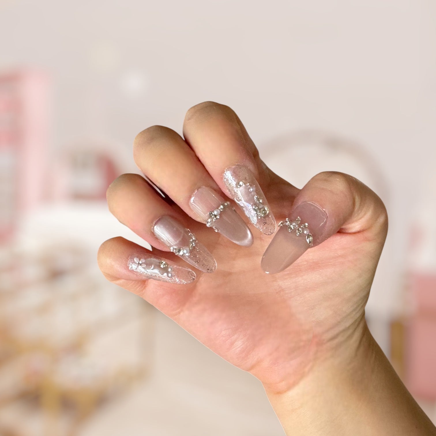 Hand with pink and clear acrylic nails with glitter accents on a blurred background