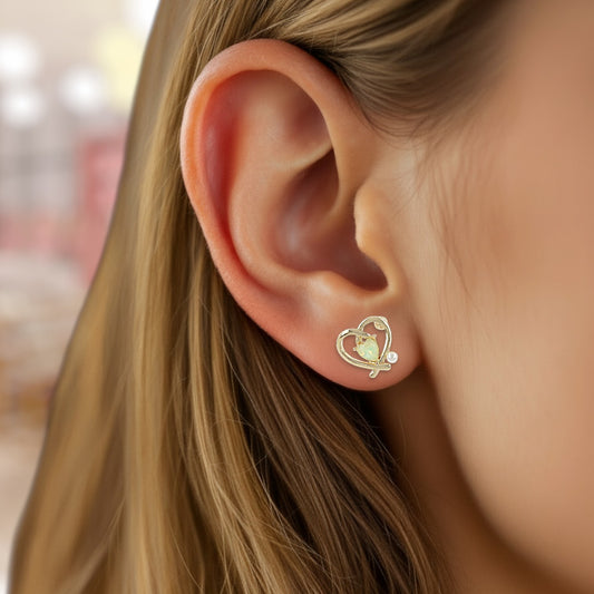 Close-up of an ear wearing a gold heart-shaped earring with a small charm.