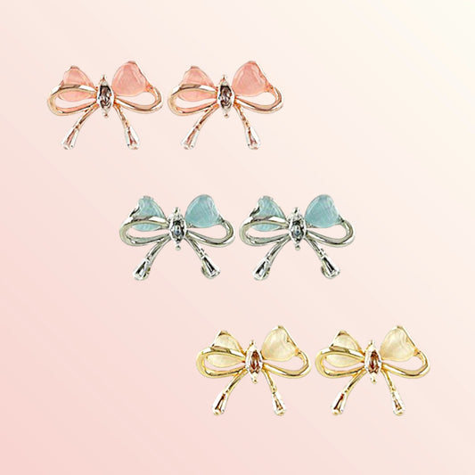 Set of bow-shaped earrings in pink, blue, and yellow on a light pink background