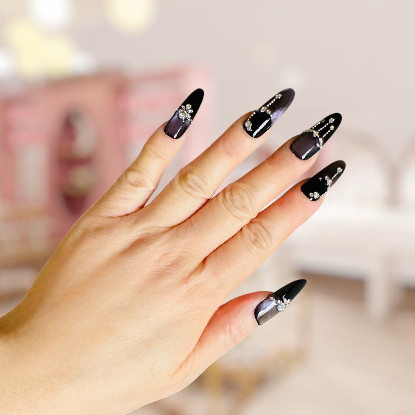 Hand with black nail art featuring rhinestones against a blurred background