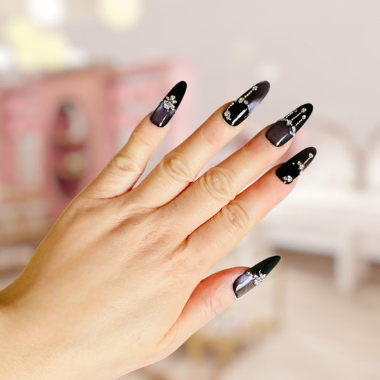 Hand with black nail art featuring rhinestones against a blurred background