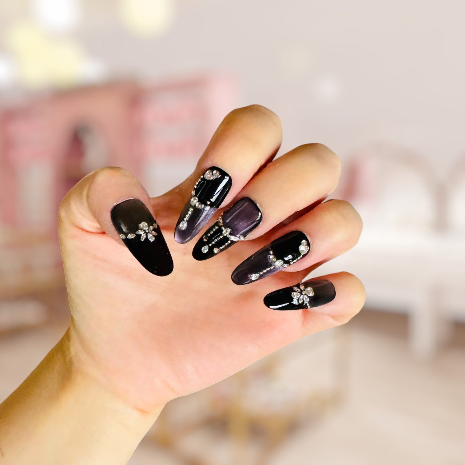 Hand with black nail art featuring decorative elements against a blurred background
