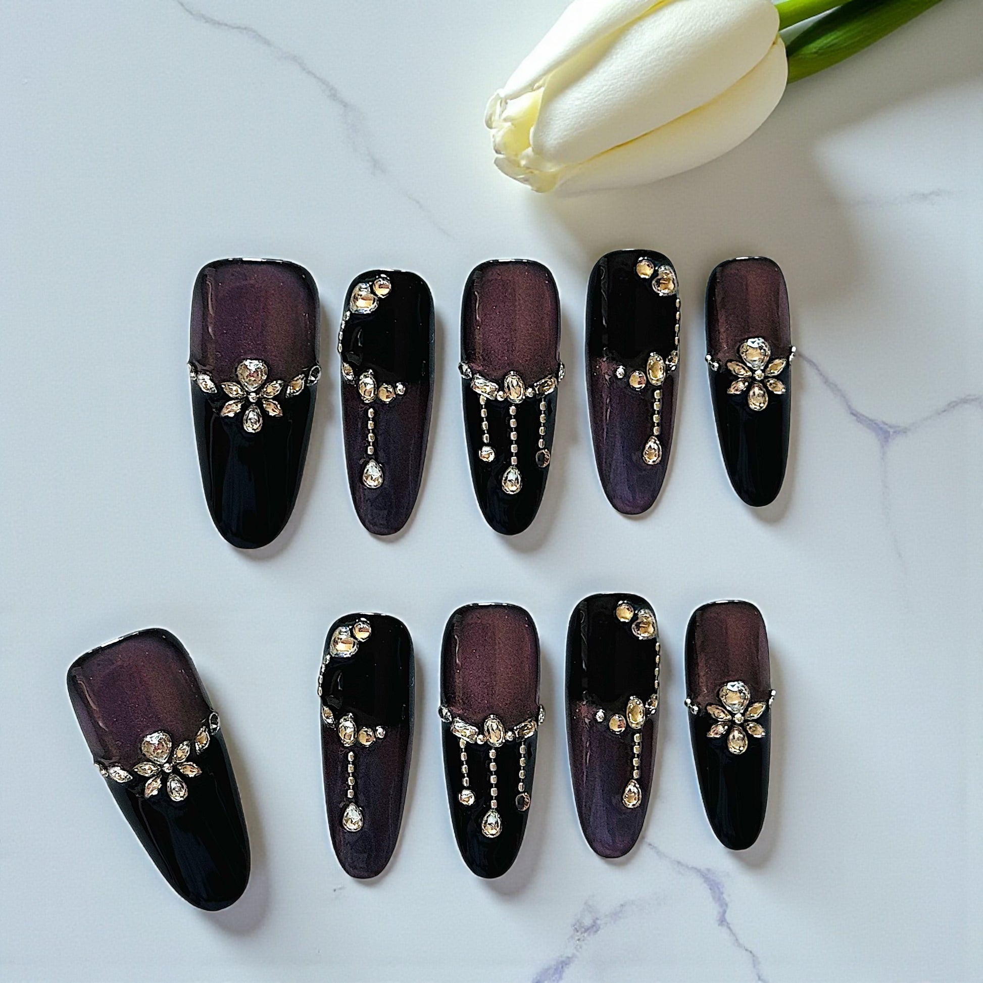 Black nail art designs with decorative elements on a marble surface with white tulips.