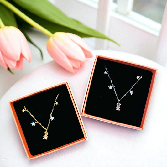 Two gold necklaces with star designs in black display boxes on a white surface with pink tulips.