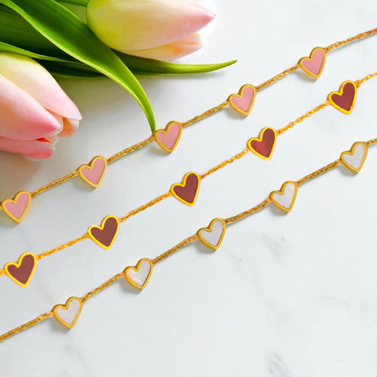 Gold chain with heart-shaped pendants next to pink tulips on a white background
