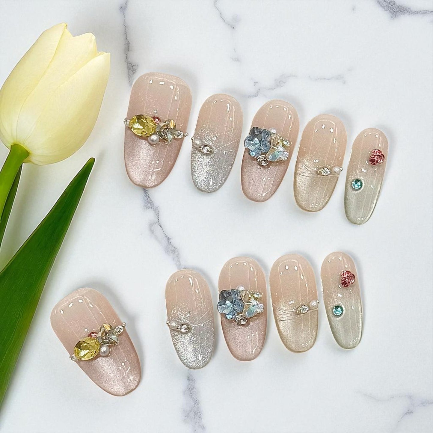Decorative nail art with gemstones on a marble surface with a tulip.