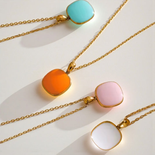 Four necklaces with colorful pendants on gold chains against a white background