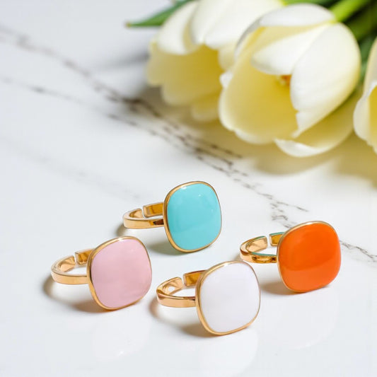 Four colorful rings on a marble surface with white tulips in the background
