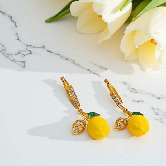 Gold earrings with yellow lemon elements on a marble surface with white tulips.
