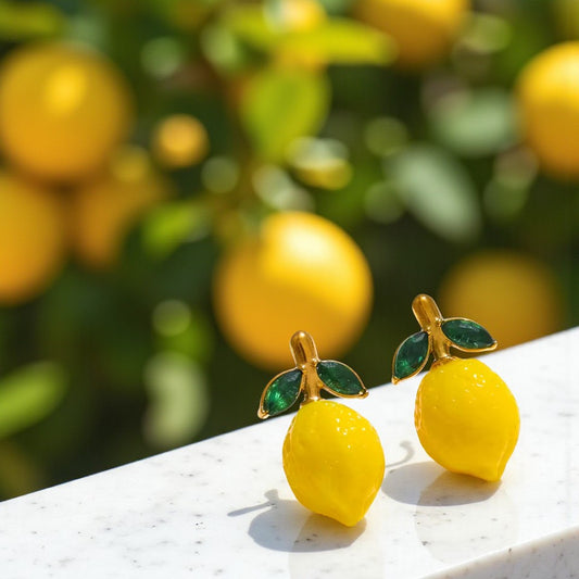 Lemon-shaped earrings with green leaves on a white surface with lemons in the background