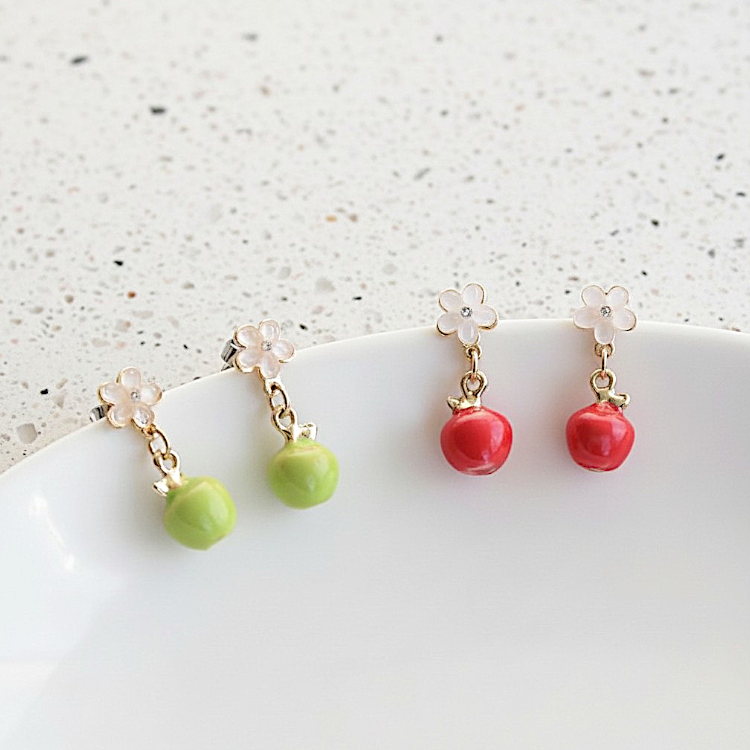 Pair of earrings with green and red fruit-like charms on a white surface