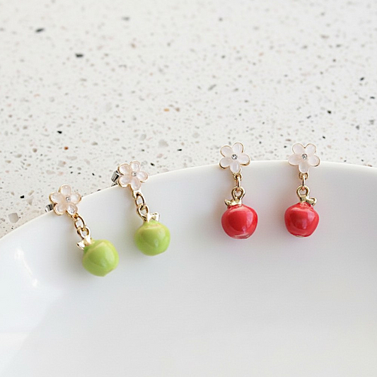 Pair of earrings with green and red fruit-like charms on a white surface