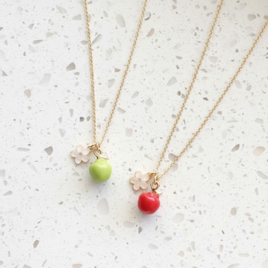 Two gold necklaces with green and red bead pendants on a light gray surface
