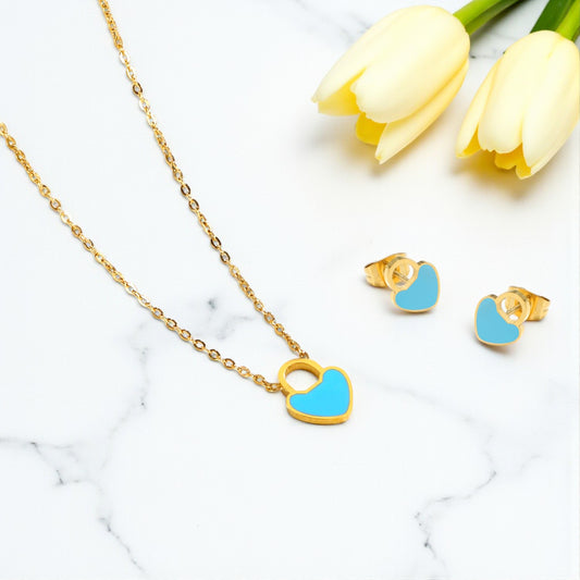 Gold necklace with blue heart pendant and matching earrings on a marble surface with yellow tulips.