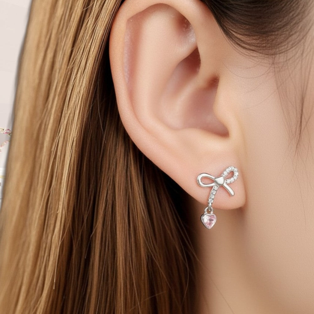 Silver bow-shaped earring with a heart detail worn by a person with long brown hair.