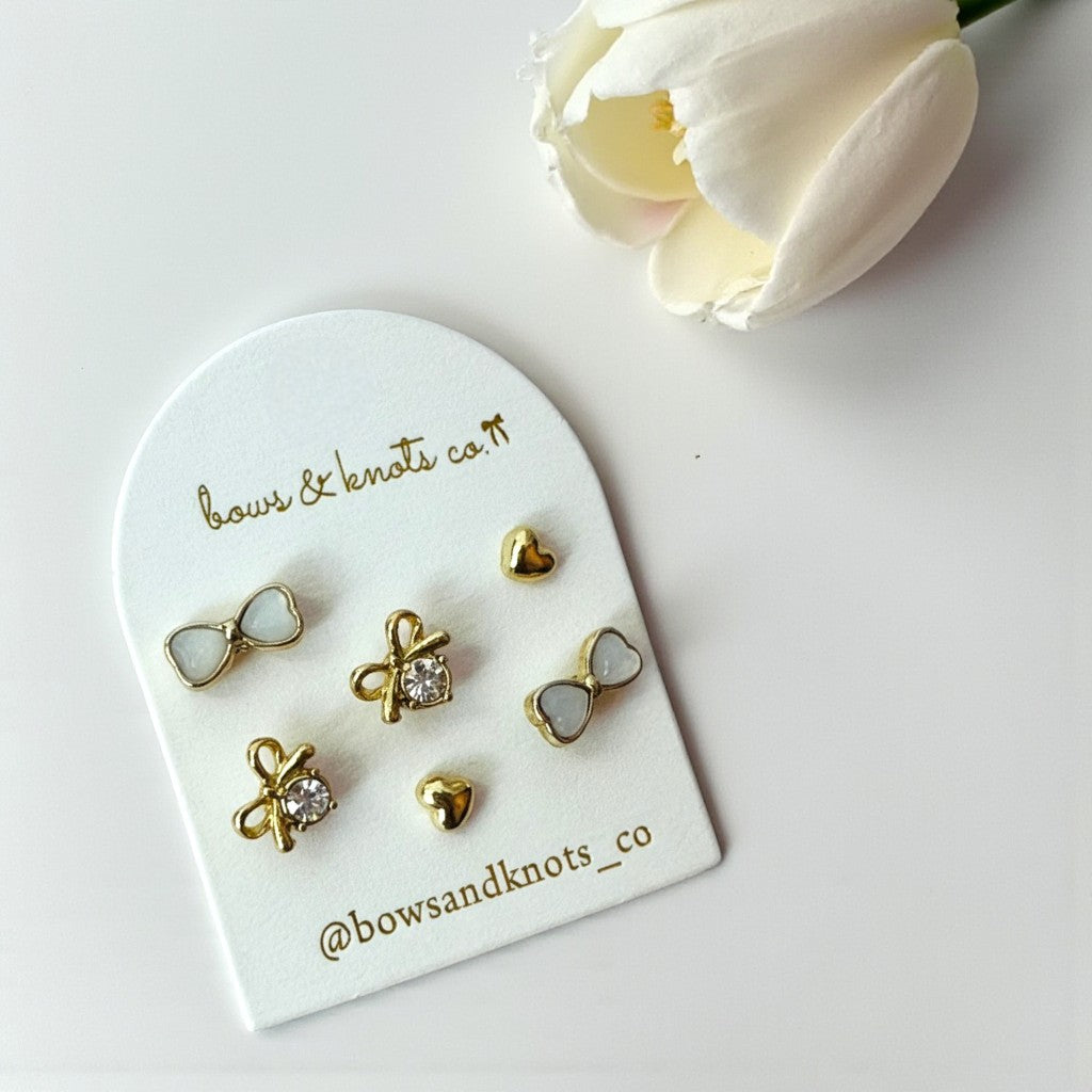 Set of gold earrings on a branded display card with a white flower in the background.