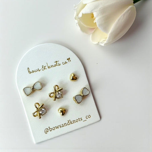 Set of gold earrings on a branded display card with a white flower in the background.