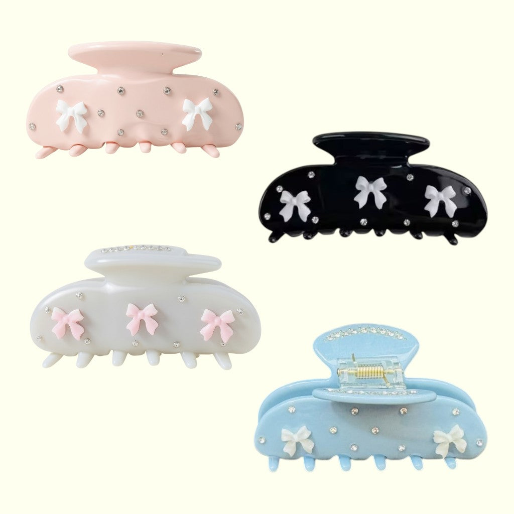 Set of four decorative hair clips in pink, black, white, and blue with bow details on a white background.
