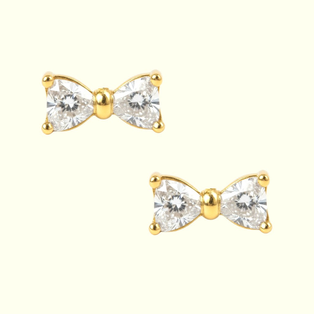 Gold bow-shaped earrings with clear gemstones on a white background